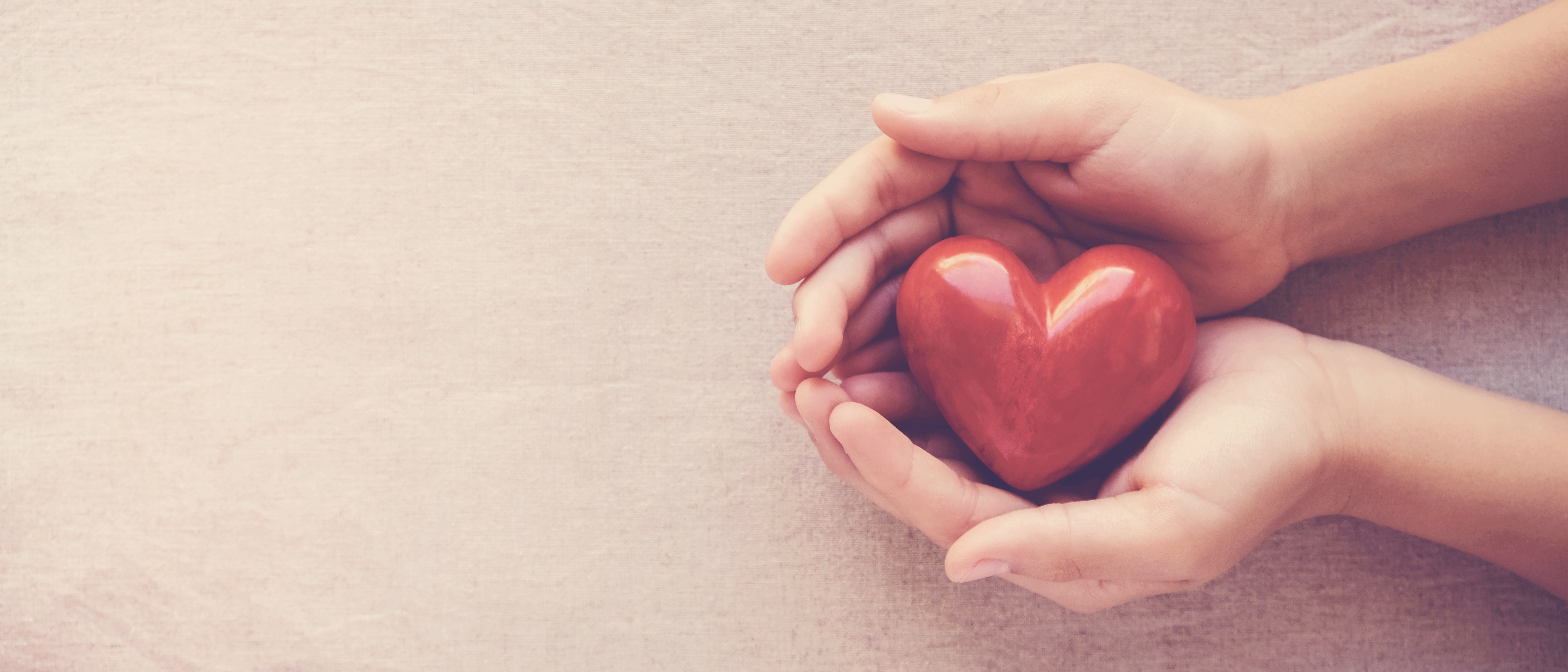 A pair of hands holding a red heart shaped ornament