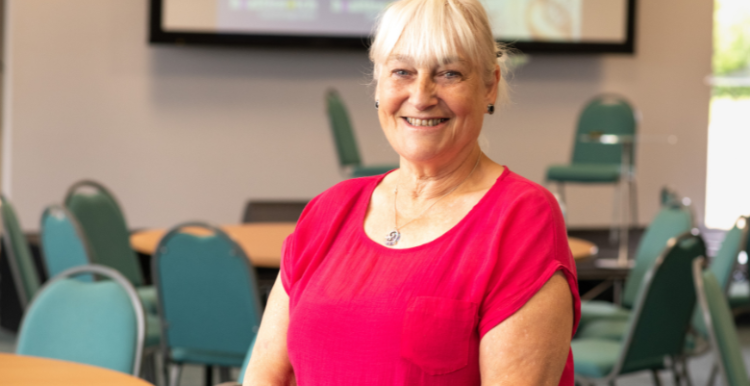 Sandie Smith, CEO, wearing a pink top, inside, standing, smiling at camera 