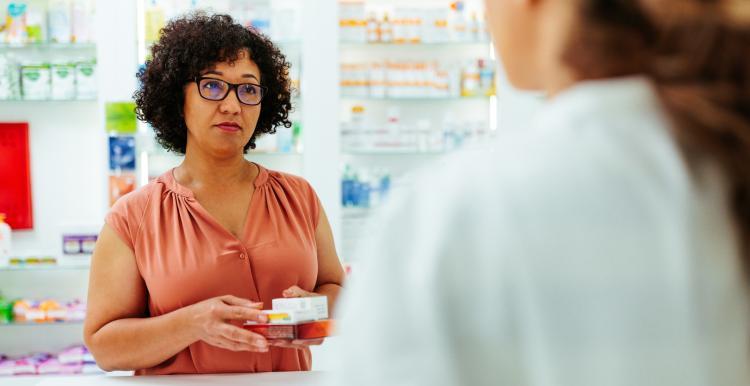 a photo of a woman in a pharmacy, holding medication in her hand