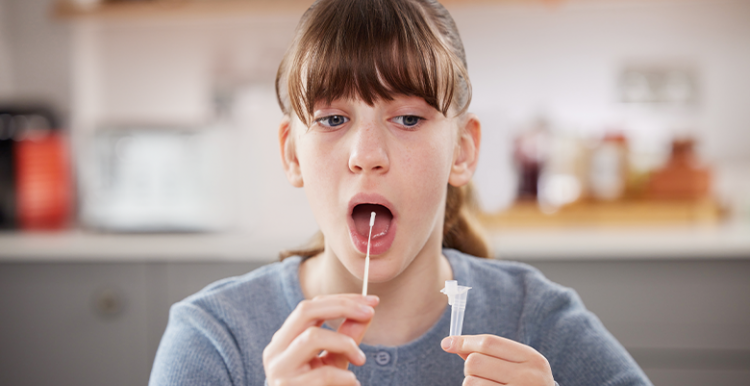 Picture shows teenage girl swabbing the back of her throat as part of a lateral flow test 