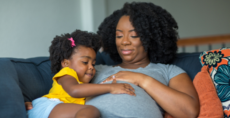 Pregnant woman and young daughter sitting on couch