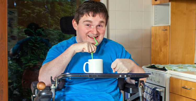 Picture shows man in wheelchair in his kitchen having a drink using a straw