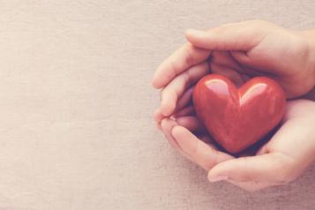 A pair of hands holding a red heart shaped ornament