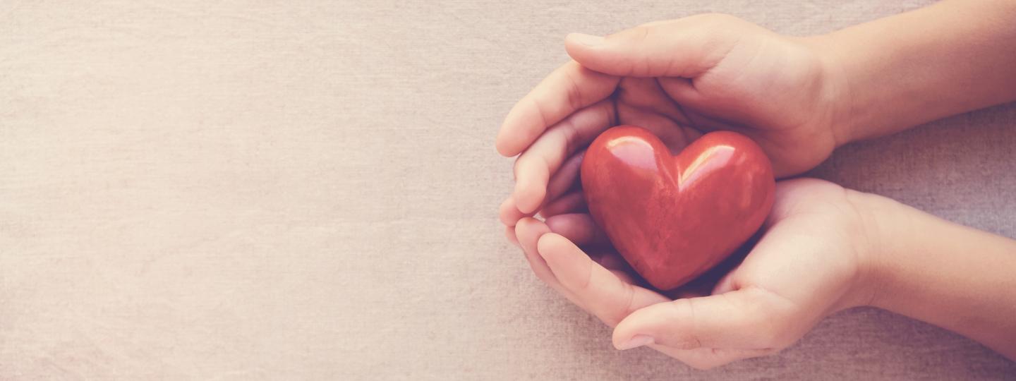 A pair of hands holding a red heart shaped ornament